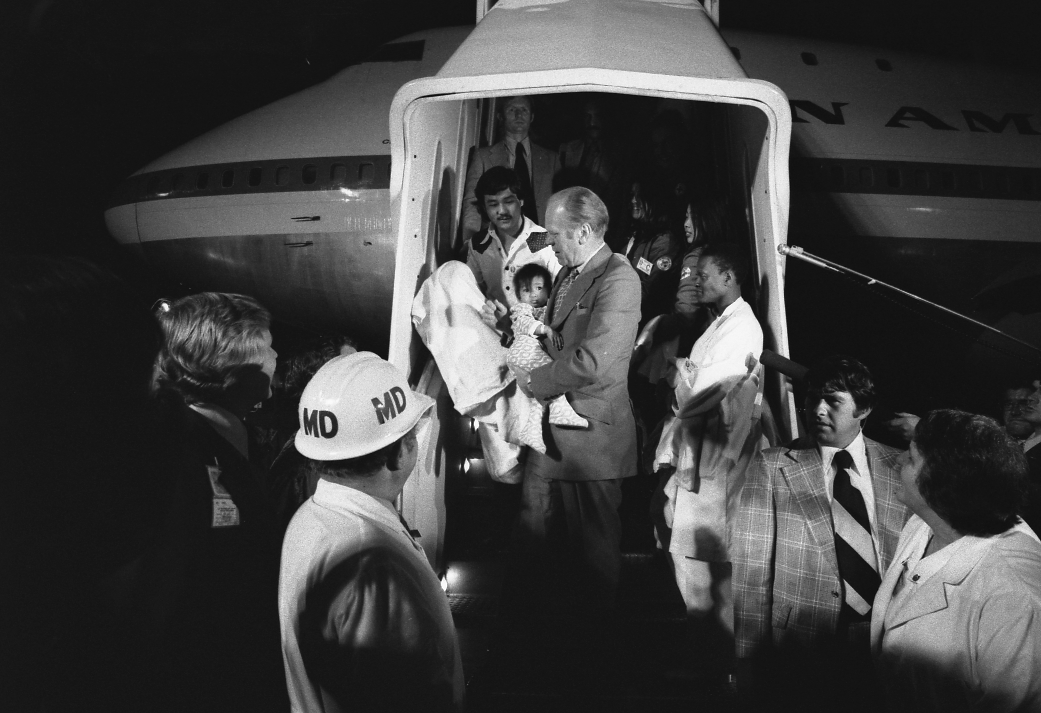 President Gerald R. Ford holds a child surrounded by airline personnel in front of an airplane