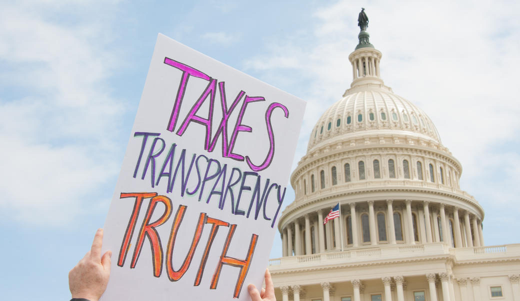 Protestor holding sign reading, "Taxes, transparency, truth" in front of the US Capitol building